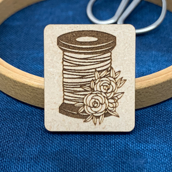 Needle minder featuring a thread spool and flowers.