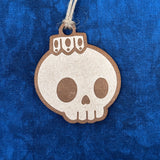 Unpainted Creepy Christmas skull bulb ornament hanging on a Christmas laying on a blue background.