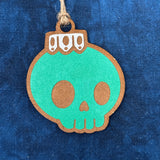 Green Hand-painted Creepy Christmas skull bulb ornament hanging on a Christmas laying on a blue background.