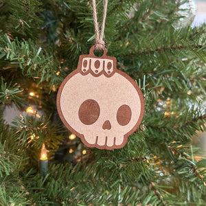 Unpainted and Hand-painted Creepy Christmas skull bulb ornament hanging on a Christmas laying on a blue background.