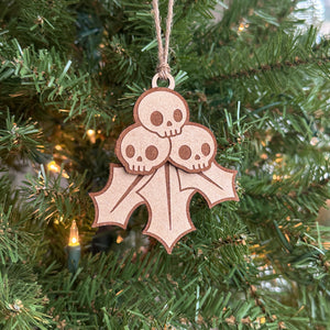 Hand-painted and unpainted Creepy Christmas Skull Holly Berry laser cut wood ornament laying on a blue background.