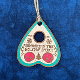 Hand-painted Summoning the Holiday Spirit Oija Planchette Ornament on a blue background.